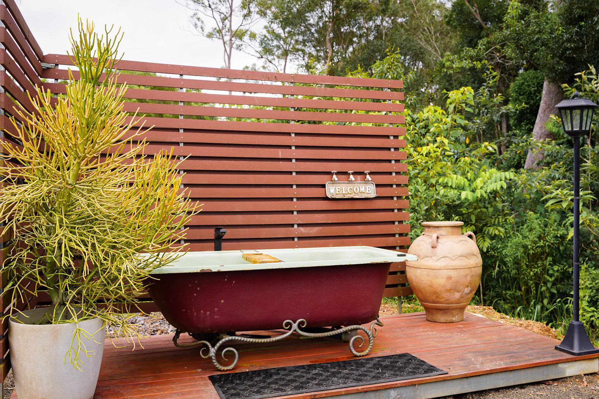 A charming vintage outdoor bathtub with ornate legs, set against a wooden privacy screen, surrounded by lush greenery at Hitching Rail Retreat